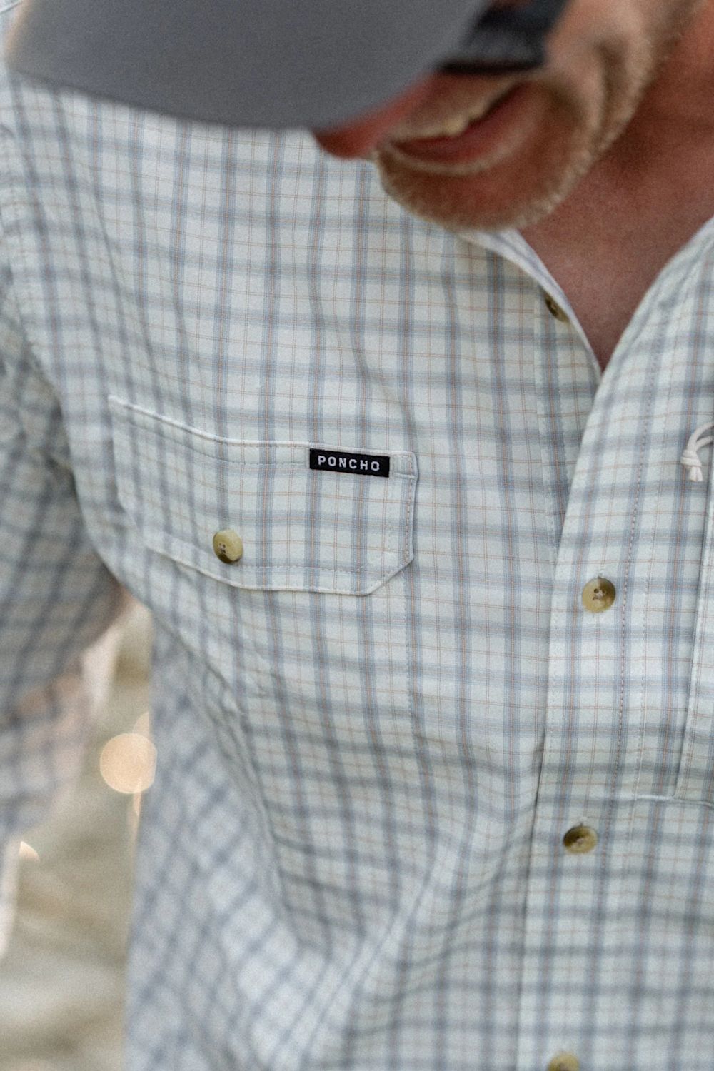 Close-up of a man wearing a light blue and white plaid button-down shirt with a chest pocket featuring a black PRINCIO label.
