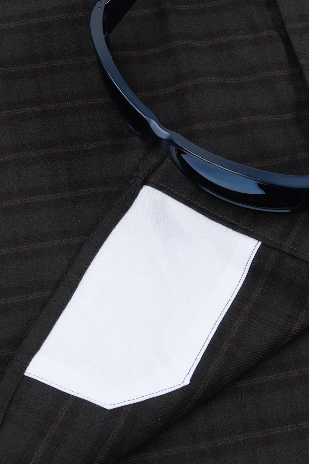 Close-up of a dark brown and black plaid suit jacket with a white pocket lining, featuring a pair of black sunglasses resting on the lapel.