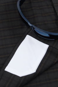 Close-up of a dark brown and black plaid suit jacket with a white pocket lining, featuring a pair of black sunglasses resting on the lapel.