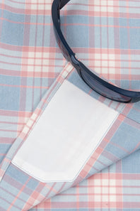 A close-up of a light blue, pink, and white plaid shirt with a white pocket flap, styled with a pair of dark sunglasses.