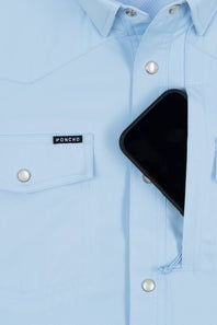 A close-up of a light blue button-down shirt with a visible PONCHO brand label on the chest pocket, featuring a black smartphone tucked into the right front pocket.