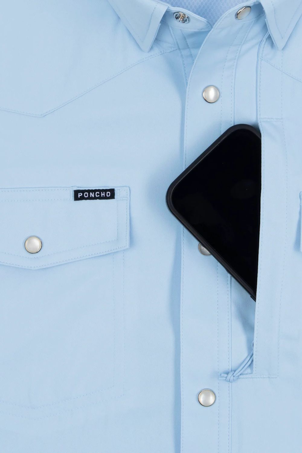 A close-up of a light blue button-down shirt with a visible PONCHO brand label on the chest pocket, featuring a black smartphone tucked into the right front pocket.