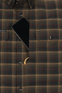 Close-up of a plaid button-up shirt in dark olive green, tan, and red, with a black smartphone tucked into the chest pocket and a small tan drawstring visible.