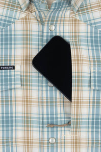 A close-up of a light blue, beige, and white plaid button-down shirt with a black smartphone tucked into the chest pocket. A small black 'PONCHO' brand label is visible on the left chest pocket.