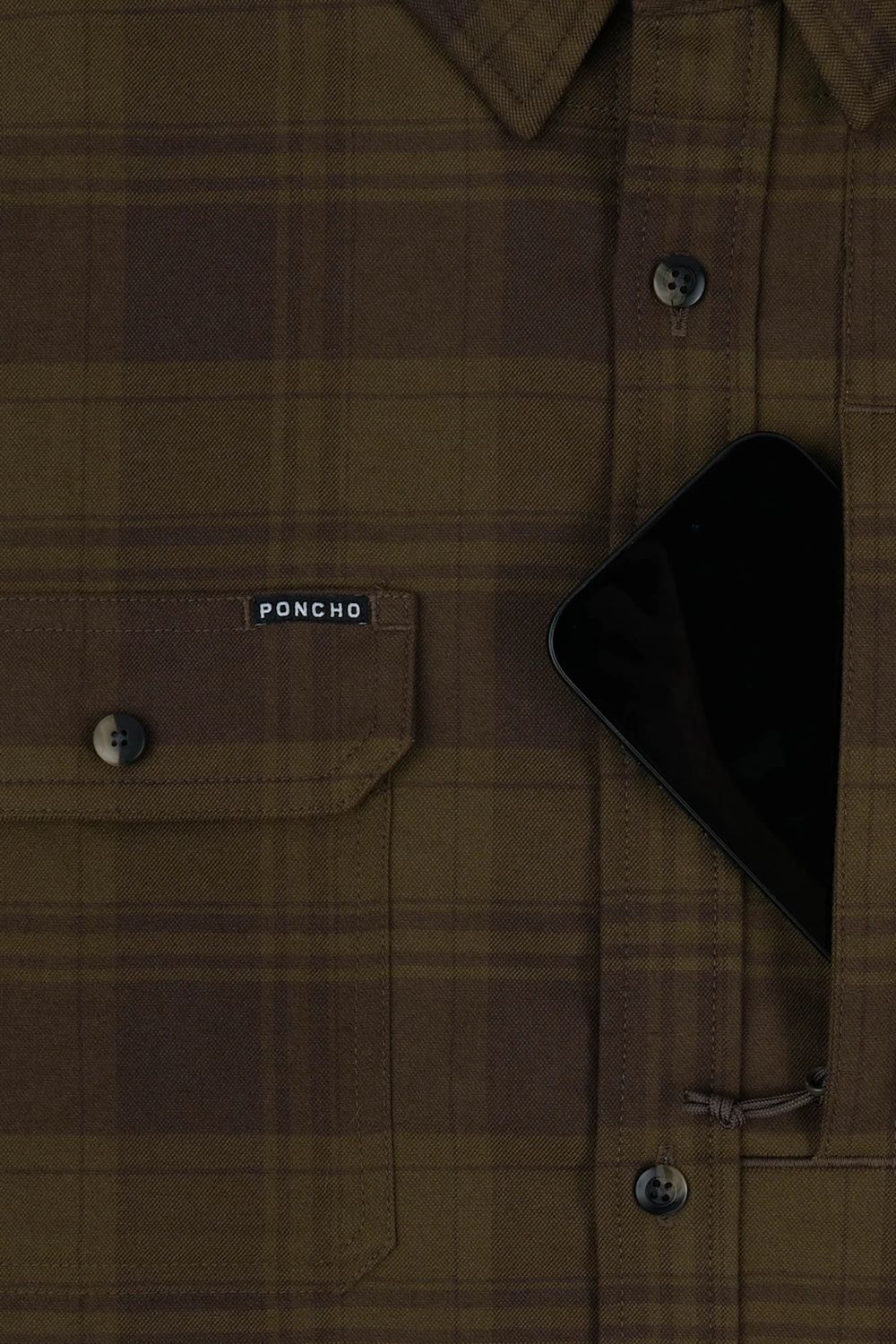 Close-up of a brown plaid button-up shirt with a chest pocket and a small visible PONCHO label, with a black phone partially tucked into the right pocket.