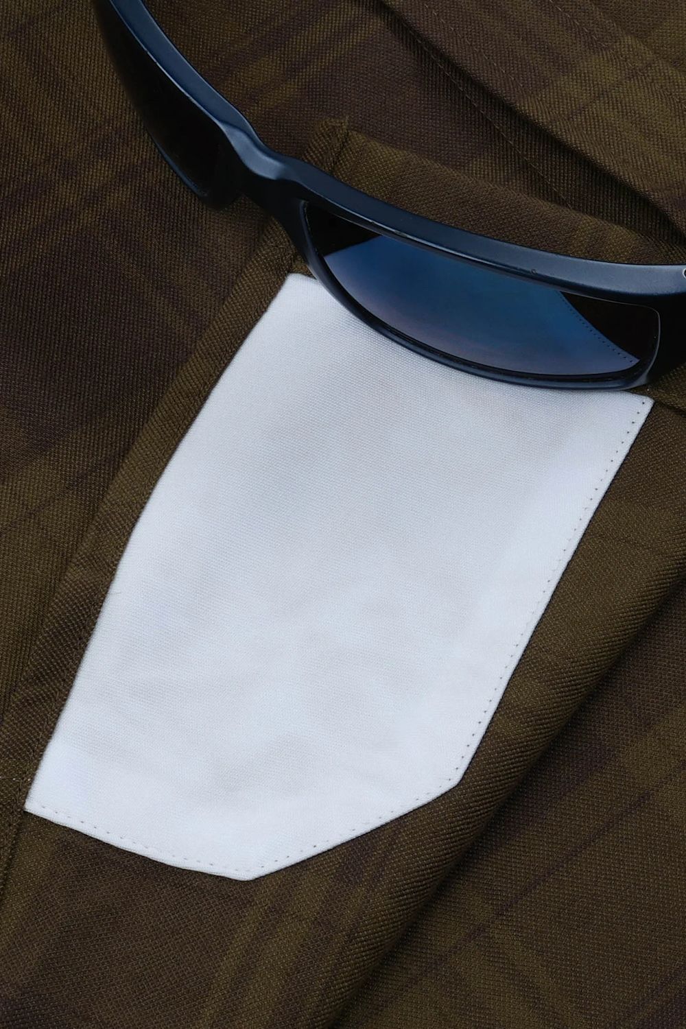 A close-up of a brown plaid jacket with a white shirt cuff peeking out, styled with a pair of dark sunglasses.