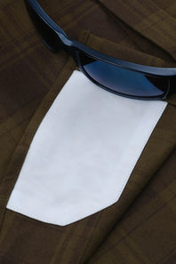 A close-up of a brown plaid jacket with a white shirt cuff peeking out, styled with a pair of dark sunglasses.