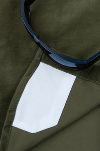 Close-up of an olive green corduroy garment with a white fabric pocket and a pair of dark sunglasses resting on top.
