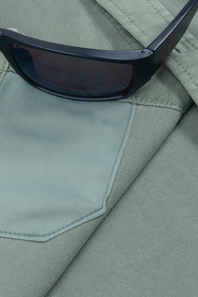 Close-up of a light sage green fabric garment with a pocket and a pair of dark sunglasses resting on it.