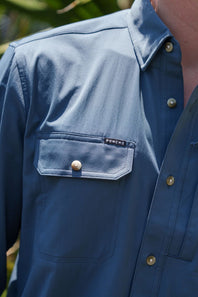 Close-up of a person wearing a blue button-up shirt with a chest pocket and a visible PONCHO label.