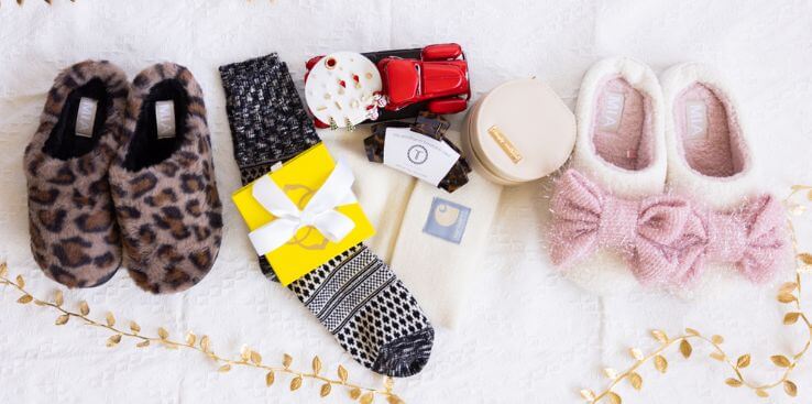 Pair of leopard print slippers, socks with patterned sole, gift box, and candle on a white surface.