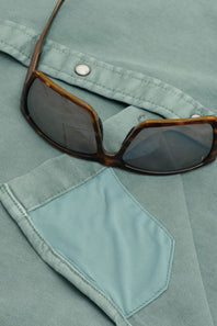 Close-up of a pair of tortoiseshell sunglasses resting on a light blue denim shirt pocket.