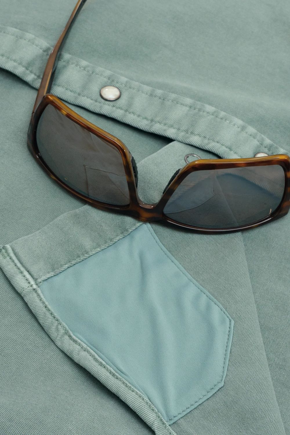 Close-up of a pair of tortoiseshell sunglasses resting on a light blue denim shirt pocket.