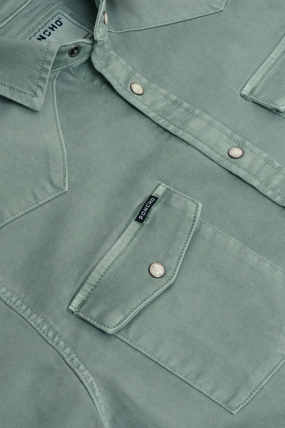 Close-up of a sage green western-style shirt jacket with silver snap buttons and a chest pocket, showing the brand label 'Poncho' on the collar 