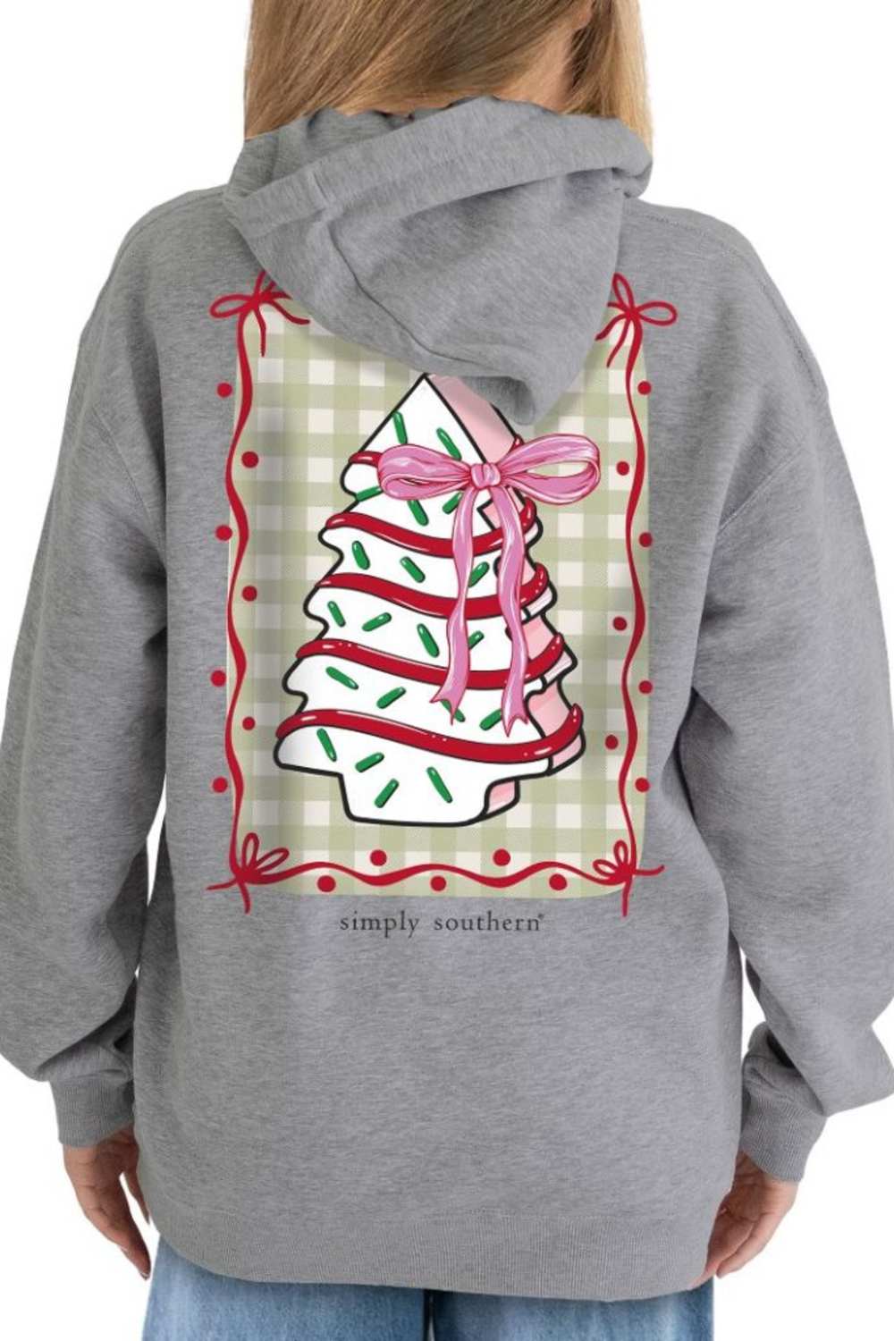 A woman wearing a heather gray hoodie from the back, featuring a large graphic of a Christmas tree wrapped in white and red striped tape with a pink ribbon, set against a beige gingham background with a red border. The brand name 'simply southern' is printed below the graphic.