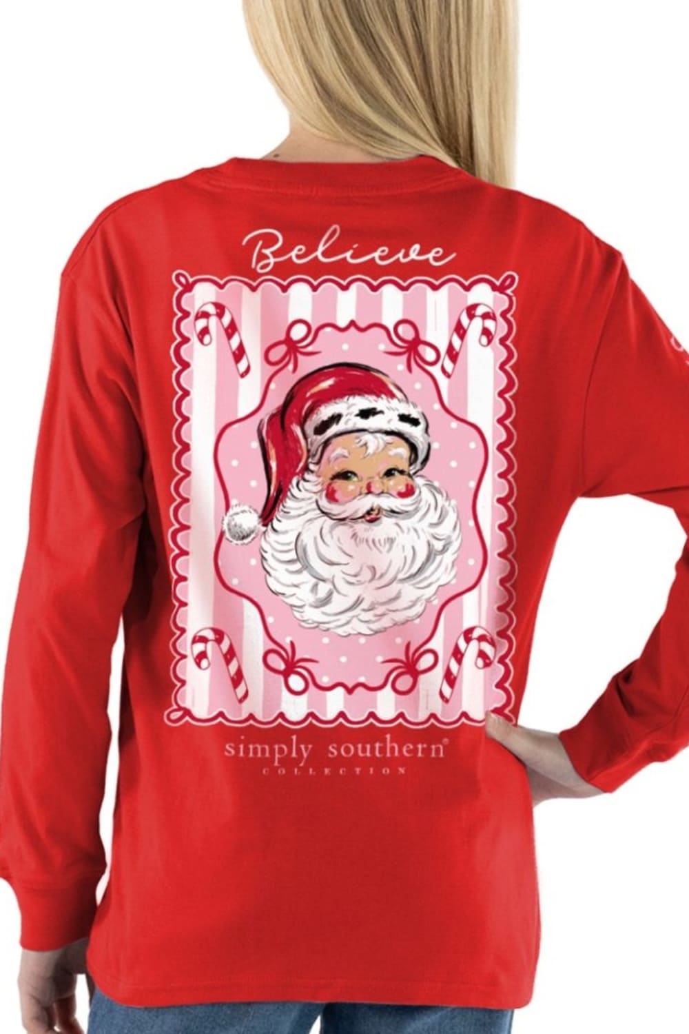 A woman shown from the back wearing a bright red long-sleeve shirt with a large Christmas-themed graphic print featuring Santa Claus and the words 'Believe' and 'simply southern'.