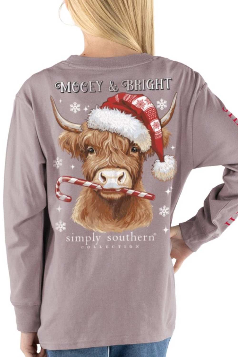A woman wearing a long-sleeve t-shirt from the back, featuring a graphic of a Highland cow wearing a Santa hat and holding a candy cane, with 'Mooey & BRIGHT' and 'simply southern' text.