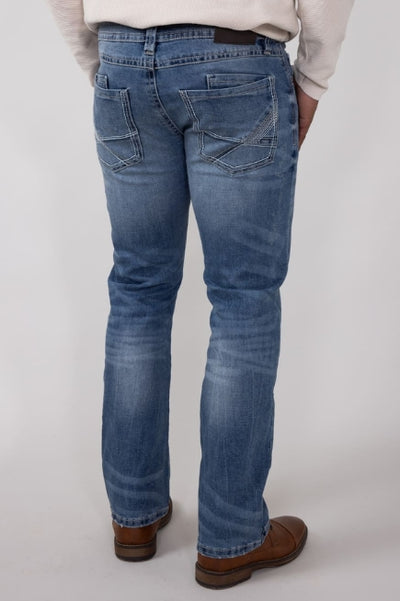 Back view of a model wearing medium-wash straight-leg jeans with stitched back pockets, paired with a light sweater and brown leather shoes against a neutral gray background.