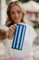 A woman holding a blue and white striped can cooler with the brand name 'KATYD' visible on the front, set against a blurred outdoor background.