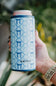 Hand holding a blue can cooler with a bow pattern and 'KATYDID' branding against a blurred natural background.