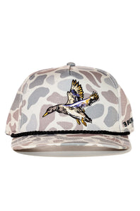 A baseball cap featuring a beige and gray camouflage pattern, a black rope detail along the brim, and a central embroidered flying duck design. The brand name 'BURLEBO' is visible on the side.