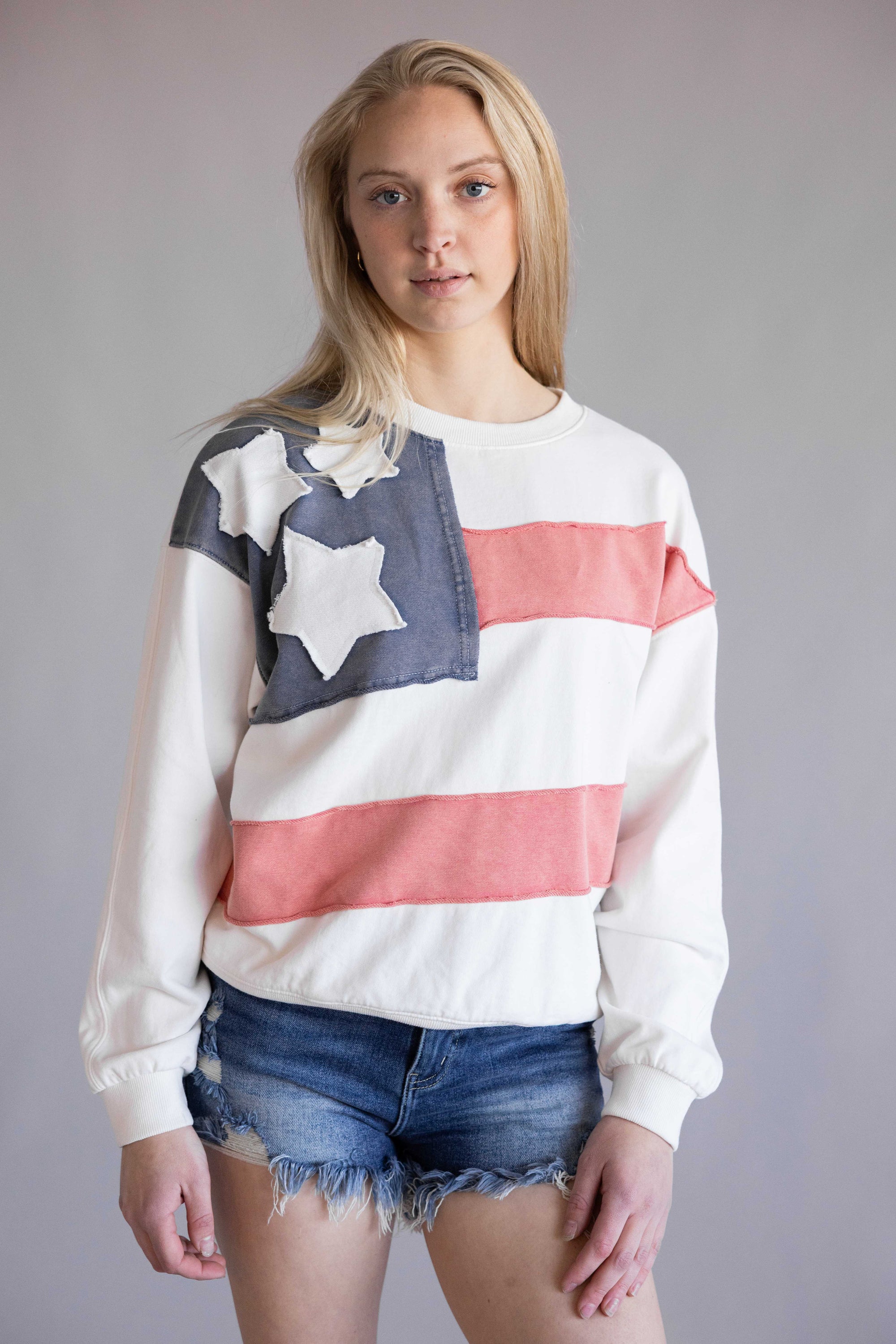 Flag USA Sweatshirt for Women in White; Person wearing a flag-themed sweatshirt with denim shorts on a plain background