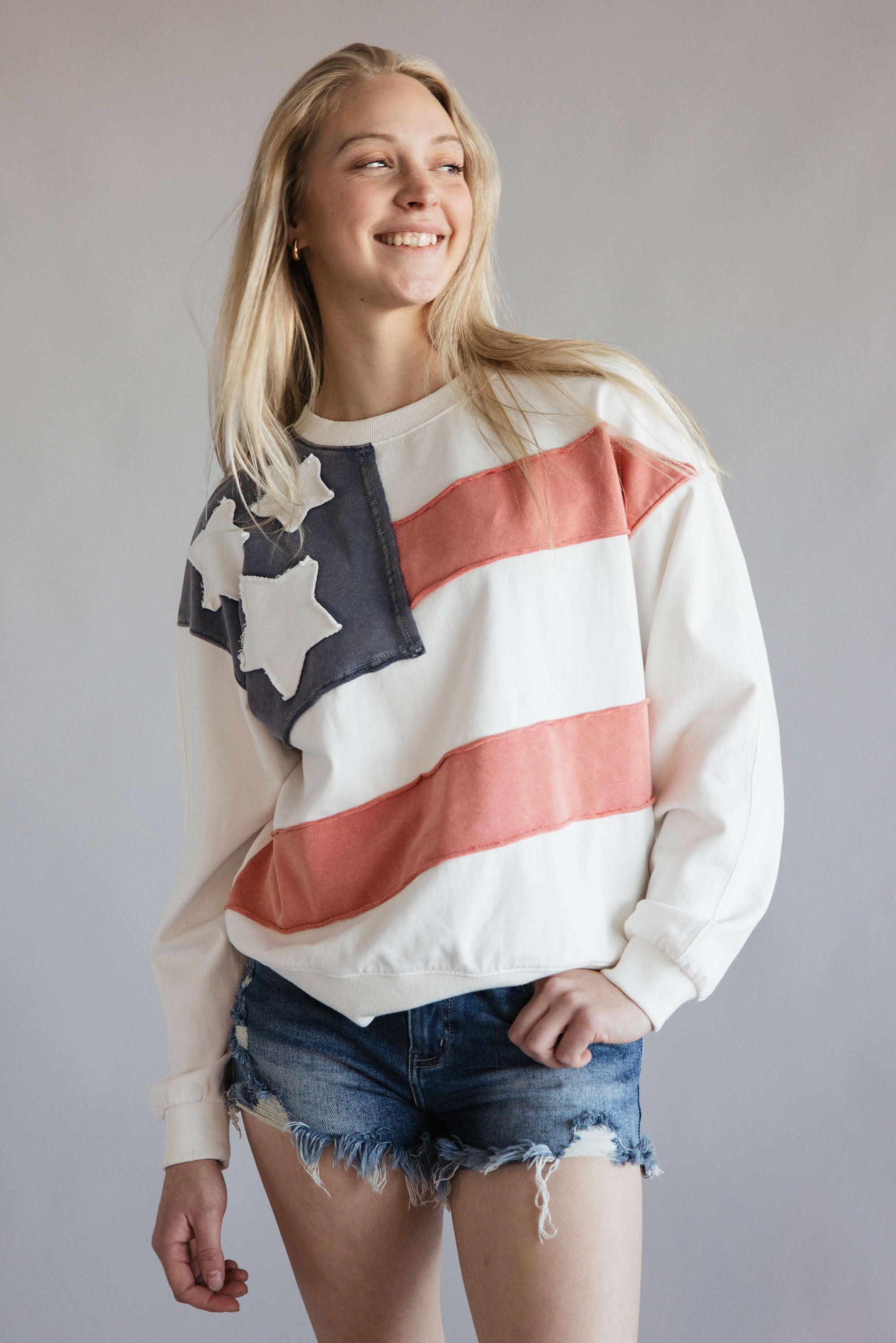 Flag USA Sweatshirt for Women in White; Woman wearing a white sweatshirt with an American flag design on a plain background