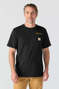 A man wearing a black Carhartt short-sleeve t-shirt with a small gold embroidered logo and the signature Carhartt square patch on the left chest, paired with tan pants, against a light gray studio background.