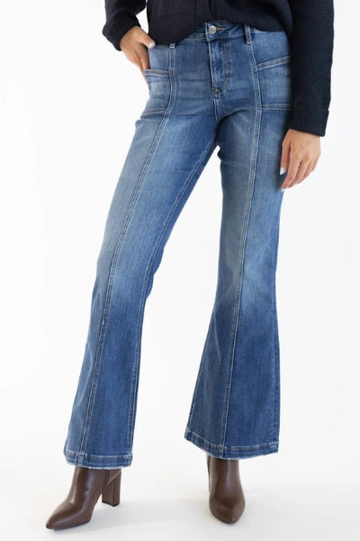 A woman wearing dark wash flare denim jeans with a black long sleeve top and brown heeled boots on a white background