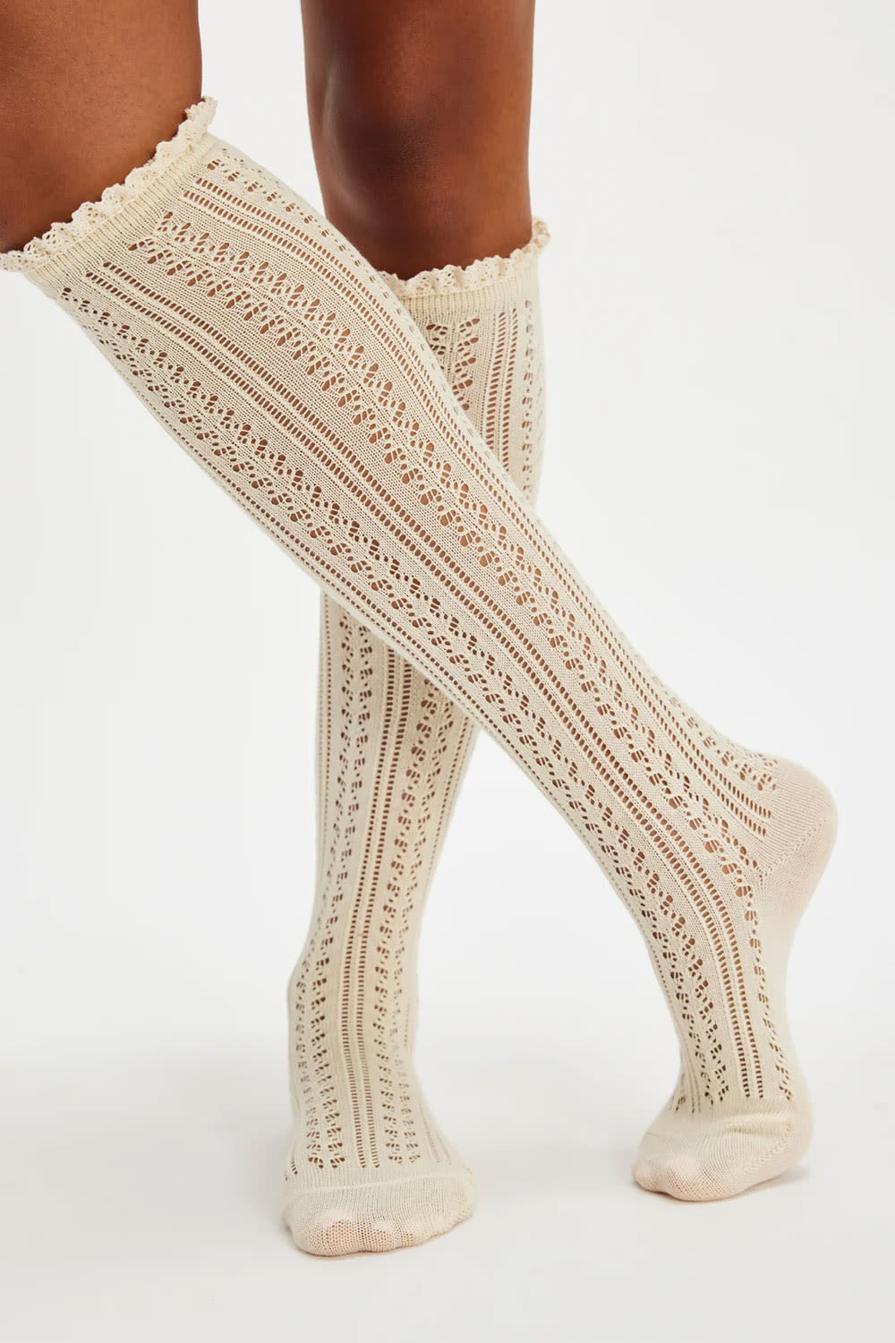 Cream-colored open-knit knee-high socks worn on a model's legs, shown against a plain white studio background.
