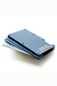 A slim black carbon-fiber-textured wallet with visible card slots holding blue, gray, and white cards, photographed on a clean white background. The brand name ARIAT is printed on the front.