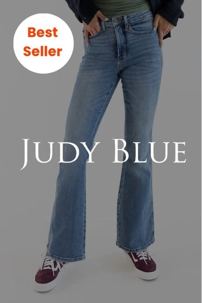 A person wearing high-waisted, medium-wash bootcut jeans and maroon sneakers with white laces. The white text JUDY BLUE is centered across the legs, and a white circular badge in the top-left corner reads Best Seller in orange text