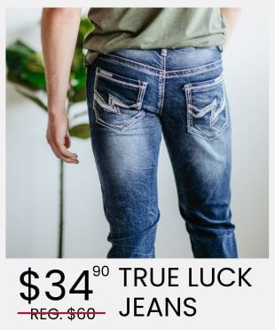 Person standing facing towards a wall wearing blue denim jeans with a promotional banner that reads $34.90 True Luck Jeans and Reg $60 strikethrough