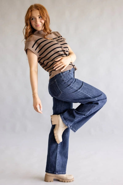 A model poses wearing dark-wash straight-leg jeans, a brown knit top with black horizontal stripes, and beige platform ankle boots against a neutral gray background.