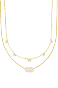 A double-strand gold necklace featuring a delicate chain with small star and bow charms set with clear stones, and a central oval pendant with a pale pink opal-like inlay, shown on a plain white background.
