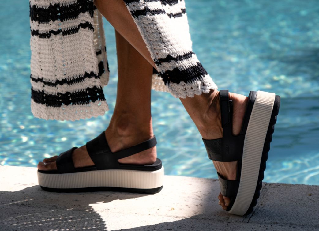Person walking near water wearing black and white platform sandals and a black and white knit style maxi dress