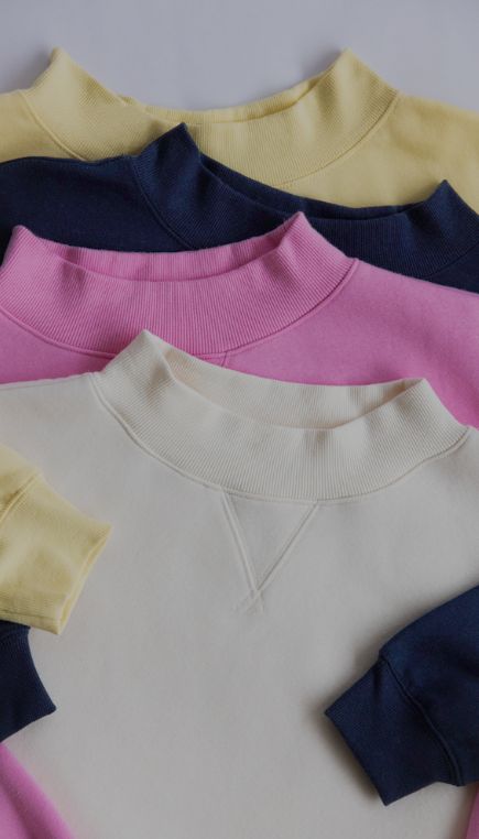 (from top to bottom) A yellow, navy, pink, and cream colored mock neck sweatshirts laying staggered on top on on another