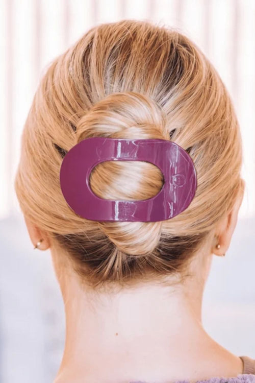 A close-up back view of a person with blonde hair styled in a low bun, secured with a glossy purple O-shaped hair claw clip.