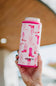 A hand holding a pink can cooler sleeve with a cowboy boot pattern, designed by Katydid.