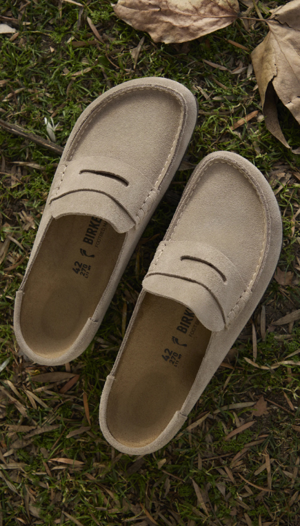 A pair of beige slip-on Birkenstock mules on grass and fallen leaves, viewed from above