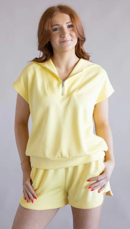 Woman wearing a yellow short sleeve quarter zip and shorts matching set on a plain background