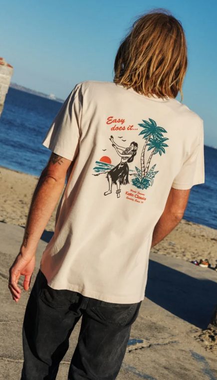 Man facing a body of water wearing a graphic t-shirt with a hula girl graphic design on the back