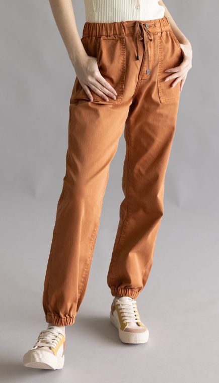Woman wearing clay orange color jogger style pants on a plain background