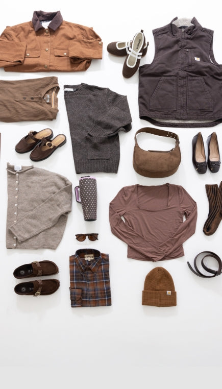 An overhead flatlay image shot from about featuring different brown product including a folded brown henley, brown mules, a light brown button cardigan, a brown long sleeve, dark brown socks, dark brown flats, a dark brown sweater, a brown and pink polka dot tumbler, dark brown vest, a brown and blue folded flannel, brown mules, a brown belt, brown and white Mary Jane shoes, and brown jacket