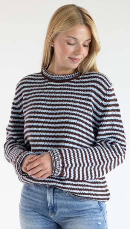 A woman wearing a blue and brown striped chunky sweaters and blue denim jeans standing against a plain background