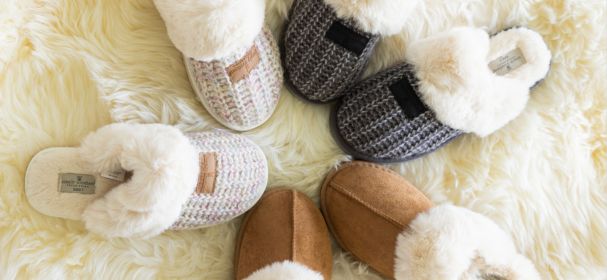 Pair of white slippers, gray slippers, brown slippers, and tan slippers on a fluffy white surface.