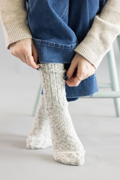 Person wearing white speckled crew socks white denim jeans standing on a clean grey floor with light green stool legs in the background