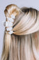 A close-up of a blonde person's hair styled with a white claw clip featuring black polka dots, shown from the back against a light gray background.