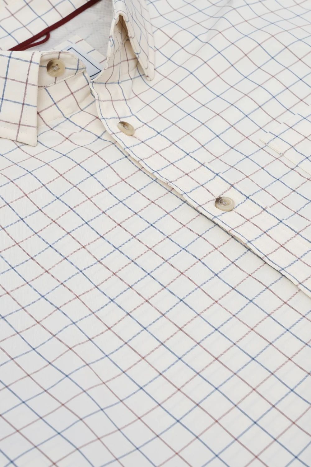 Close-up of a white button-up shirt with a fine blue and red windowpane check pattern, showing the collar, button placket, and fabric texture.