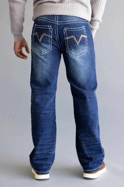 A person in a gray sweater and faded blue jeans with embroidered back pockets stands facing away on a neutral background, creating a relaxed tone.